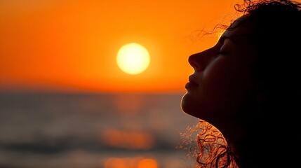 Serene profile of a woman with eyes closed against a vibrant sunset over the ocean