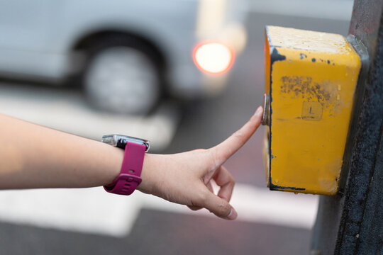 Pushing the pedestrian crossing lighting button, activate the signal for safety transportation. Close-up with selective focus on human hand.