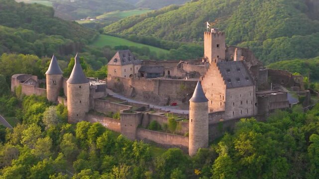 bourscheid castle ch&acirc;teau de green cover valley hills behind walls black domed towers parked visitor vehicles historic site to left around right drone panning 
