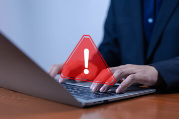 Businessman typing on laptop with red warning alert symbol, representing cybersecurity threat, data breach, computer error, system risk, and online security protection in digital technology concept.