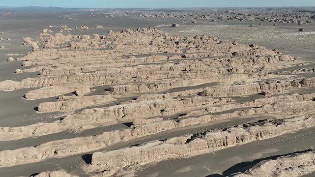 Aerial view of the Yardang landscape reveals wind-eroded ridges and mesas casting shadows on the desert floor, creating a textured, alien landscape, Gobi Desert, China.
