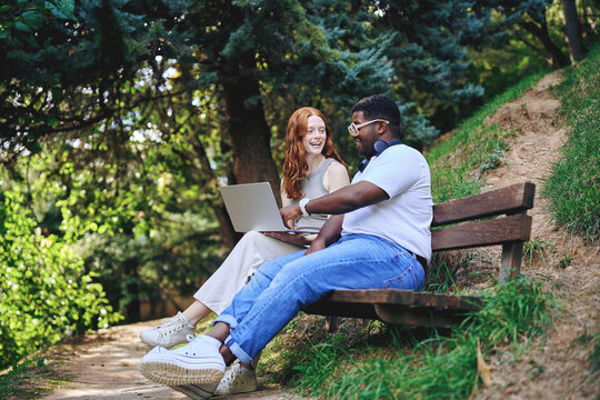 Smiling students using laptop together in park