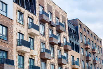 Fototapeta premium A modern residential complex with exposed brickwork, balconies, and large windows. The façade is finished in warm tones, with an emphasis on geometric shapes and stylish black railings.