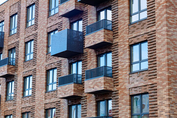 The facade of a brick building in a loft style: large windows, balconies with black metal railings, textured masonry, modern design, urban style.