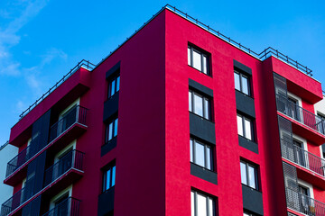 A modern residential building with a striking red façade, black accents, and minimalist balconies....
