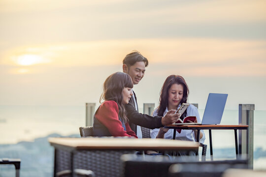 Multicultural colleagues in a friendly conversation. Business team sharing ideas checking email reading book in a casual on roof terrace. Evening sky scene with different shades light from setting sun