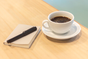 Coffee cup and notepad on a wooden table create a cozy workspace atmosphere in a cafe during the morning hours