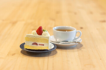 Delicious slice of cake with strawberries and cup of tea on a wooden table in a cozy cafe setting