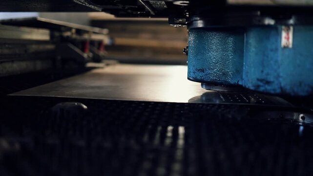 Close-up of an industrial turret punch press machine head working on a sheet metal plate, perforating holes with precision in a modern factory setting with automated technology