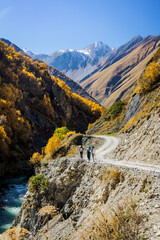 Hiking in Georgia’s Truso Valley gorge during peak autumn. Travelers exploring scenic mountain road surrounded by golden trees and rugged cliffs