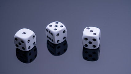Three white dice are on a black background. The dice are arranged in a row, with the middle one slightly larger than the other two. Concept of anticipation and excitement