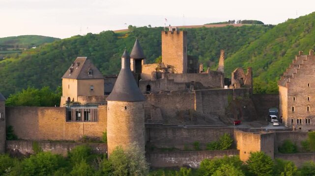 bourscheid castle ch&acirc;teau de green valley cover hills behind walls towers exterior views visitor parking vehicles to left near right up close circling drone 