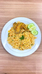 Plate of Indonesian nasi goreng with fried chicken wings and fresh cucumber slices served on wooden table top view