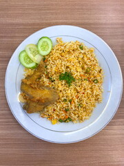 Indonesian fried rice with chicken wings and cucumber slices served on white plate over wooden table top view