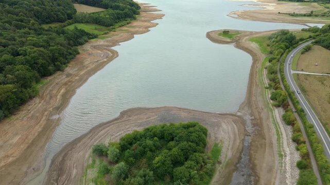 Aerial view of a river with exposed banks and a road running alongside it, contrasting the water with the surrounding greenery, Matlock, England, United Kingdom.