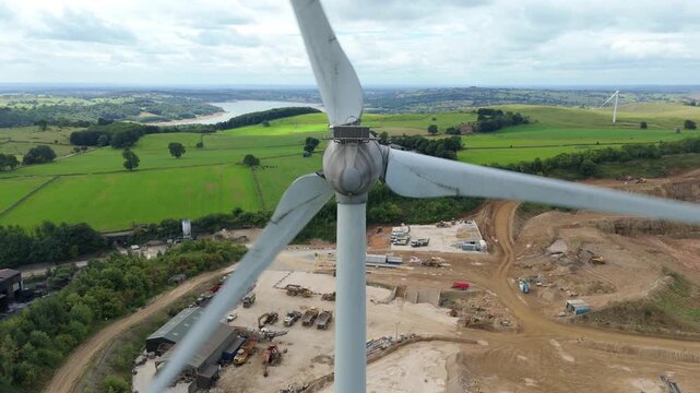 Aerial view of wind turbines standing tall over the quarry contrasting with the green fields near the lake, Matlock, England, United Kingdom.
