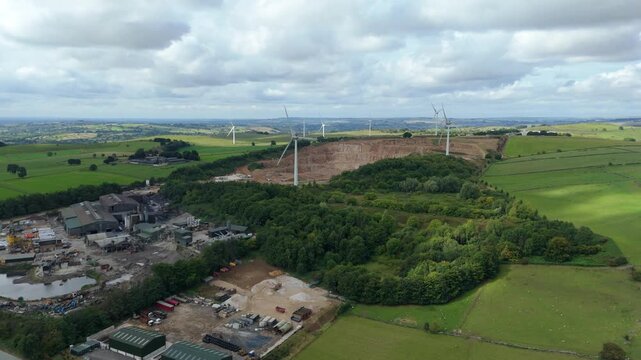 Aerial view of the landscape featuring wind turbines standing tall near an industrial area with green fields, Matlock, England, United Kingdom.