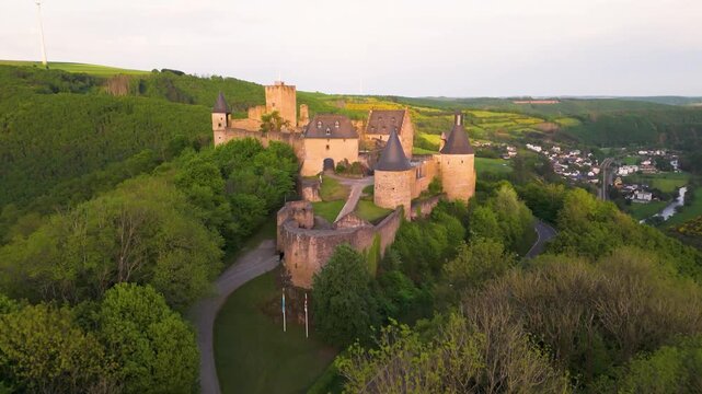 bourscheid castle ch&acirc;teau de top bottom green valley cover hills behind walls towers flags town visible to from rising closeup down aerial drone shot 