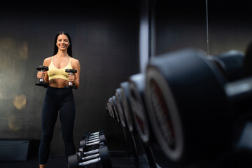 Smiling female professional gym trainee exercising with dumbbell weights.