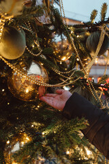 Woman's hand touching gold Christmas ball hanging on the Christmas tree, magic design on New Year and Christmas winter holidays