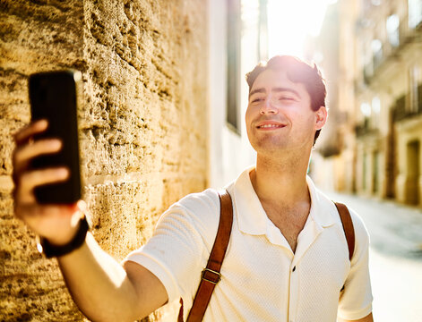 Young man enjoys sunny day while using smartphone and taking a selfie photo  in urban setting, highlighting her joy and connection to the world around her