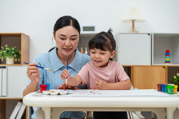 happy mother and toddler girl painting watercolor in paper at home