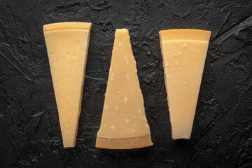Parmesan cheese wedges, overhead flat lay shot, on a black slate background, an assortment
