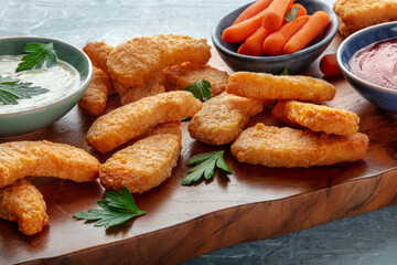 Chicken nuggets with fresh vegetables and dips, a close-op on a wooden board, a healthier fast food dinner