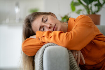 Middle-aged woman deeply tired and asleep on home sofa born from emotional exhaustion and chronic...