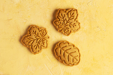 Honey or gingerbread cookies shaped like autumn leaves on yellow background. Maple and oak leaves made from shortcrust pastry. Copy space. Autumn baking