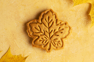 Honey or gingerbread cookies shaped like autumn leaves on yellow background. Maple and oak leaves made from shortcrust pastry. Copy space. Autumn baking