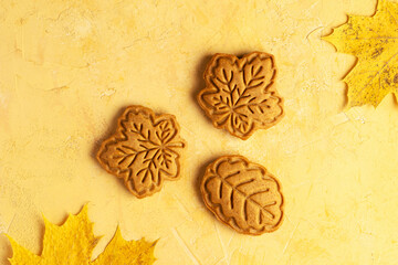 Three honey or gingerbread cookies shaped like maple leaves on yellow background. Autumn cookies made from shortcrust pastry