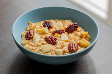 creamy pumpkin oatmeal topped with fresh apple slices and caramelized pecans