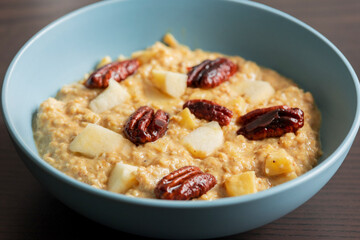 creamy pumpkin oatmeal topped with fresh apple slices and caramelized pecans