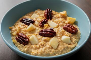 creamy pumpkin oatmeal topped with fresh apple slices and caramelized pecans