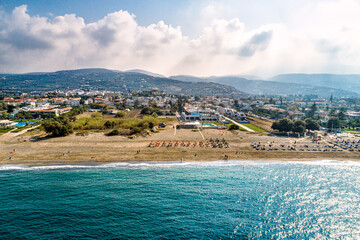Aerial view of coastal town with sandy beach, turquoise sea, and mountains in distance. Seaside resorts, sunbeds, and calm waves create perfect Mediterranean holiday atmosphere.