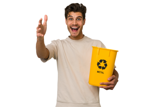 Young caucasian man holding a metal trash for recycle Young caucasian man holding recycling bins isolated on white background receiving a pleasant surprise, excited and raising hands. - Powered by Adobe