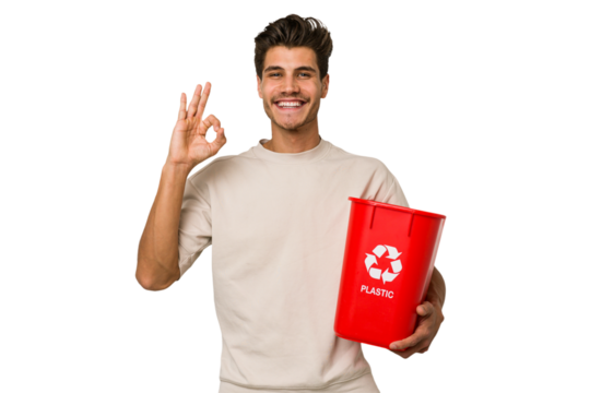 Young caucasian man holding a plastic trash isolated cheerful and confident showing ok gesture.