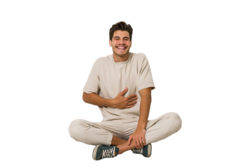 Young caucasian man sitting on the floor isolated on white background touches tummy, smiles gently, eating and satisfaction concept.