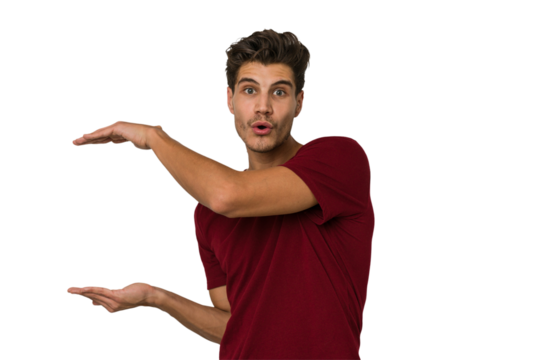 Young handsome caucasian man isolated on white background shocked and amazed holding a copy space between hands.