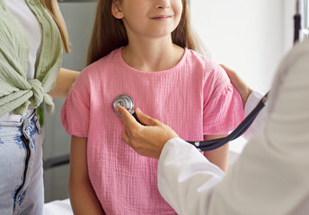 Pediatrician places stethoscope on child during checkup. In the clinic, a close-up exam shows...