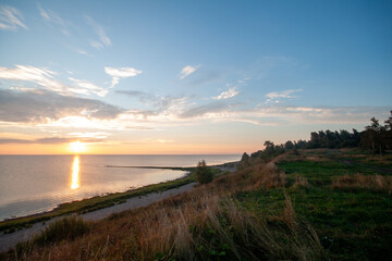 A serene sunset with a calm sea and sandy beach in the foreground.