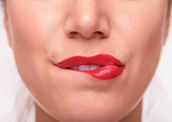Fototapeta premium Close-up of a womans lips with bright red lipstick, showing a playful and sensual expression as she bites her lower lip.