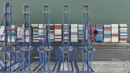 Xiamen, China - 17 September 2025: Aerial view of several blue cranes stand tall against the backdrop of a ship loaded with colorful containers.