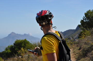 Cyclist using smartphone while resting on mountain trail with scenic landscape view