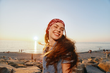 smiling woman enjoying sunset on rocky beach with ocean waves and warm sunlight in summer evening outdoors