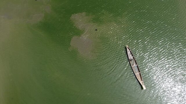 Makurdi, Nigeria - 13 October 2025: Aerial view of a single boat cutting through the green water of the Benue River, creating ripples in its wake.