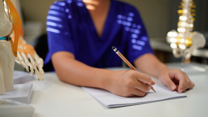 Doctor taking notes in office with spine model for diagnosis