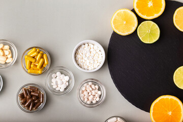 Various nutritional supplements, vitamins and minerals, pills and tablets, citrus fruits - lemon, orange and lime on black stone desk on grey background from above. Natural vitamins from fruits