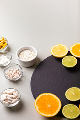 Various nutritional supplements, vitamins and minerals, pills and tablets, citrus fruits - lemon, orange and lime on black stone desk on grey background from above. Natural vitamins from fruits